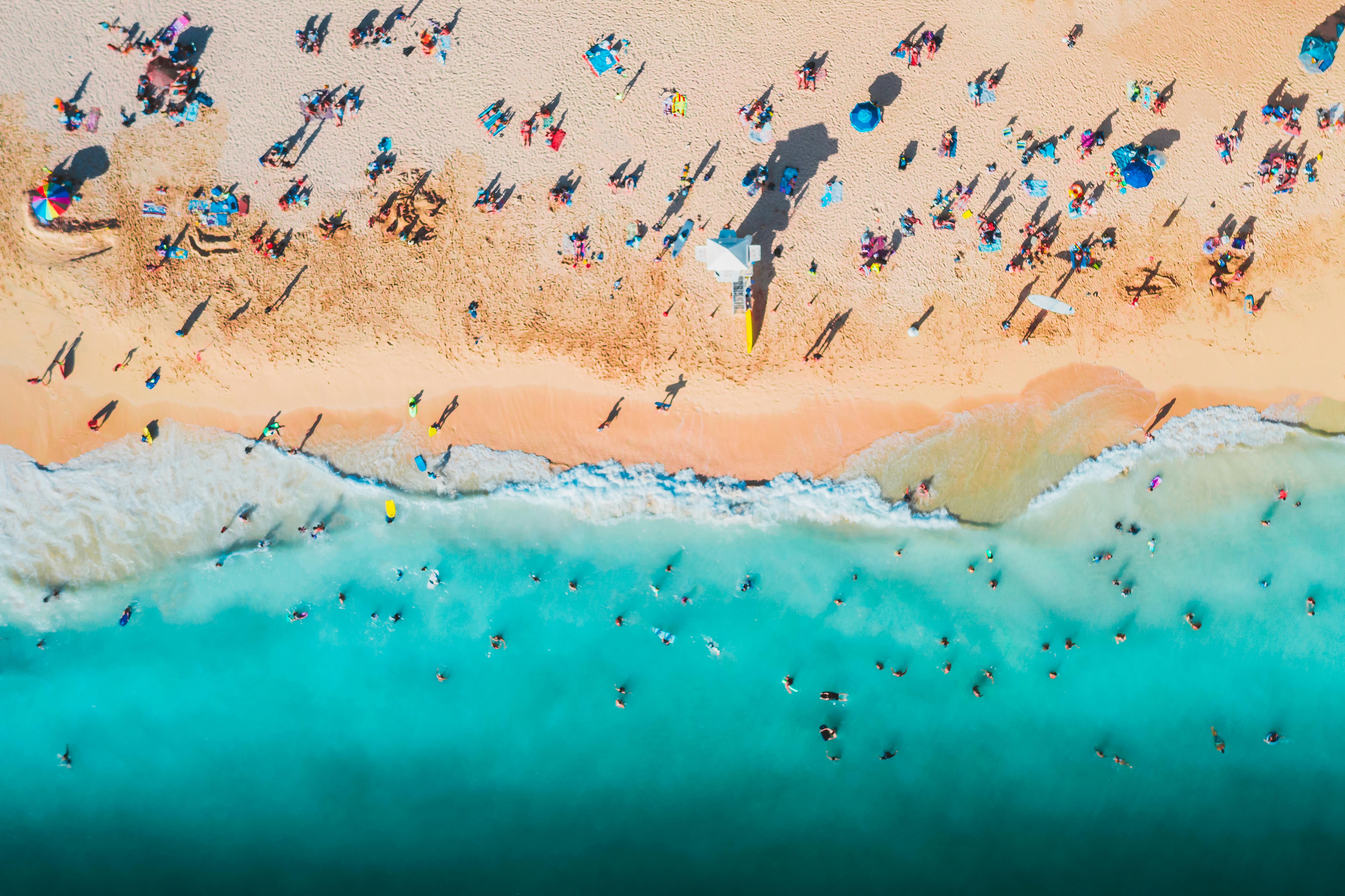 Overhead view of many tourists crowding a beach’s shores and waters.