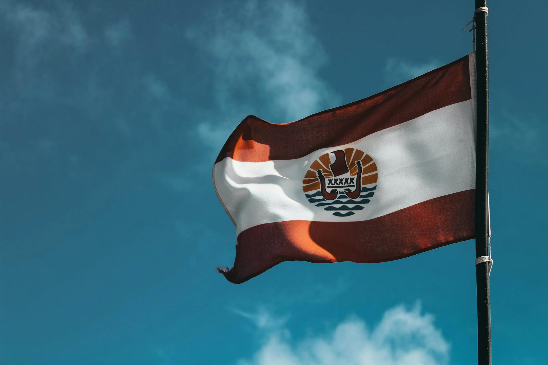 The Polynesian flag hoisted on a flagpole against the backdrop of a clear, blue sky