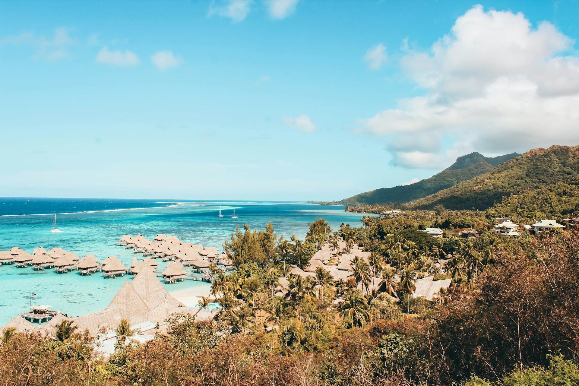 The view of a beach with overwater bungalows surrounded by mountains and palm trees