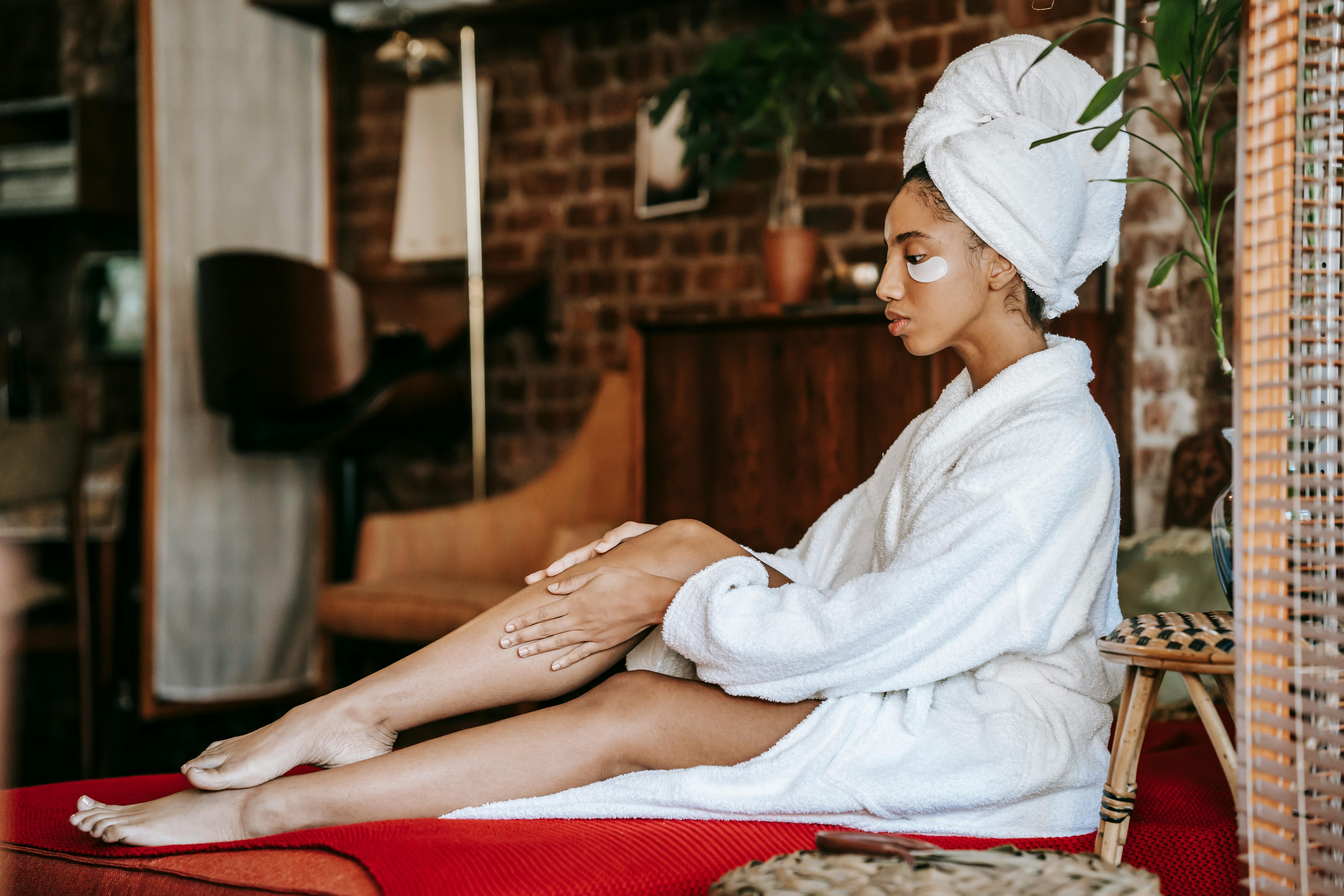 Woman in a bathrobe applying lotion on her leg