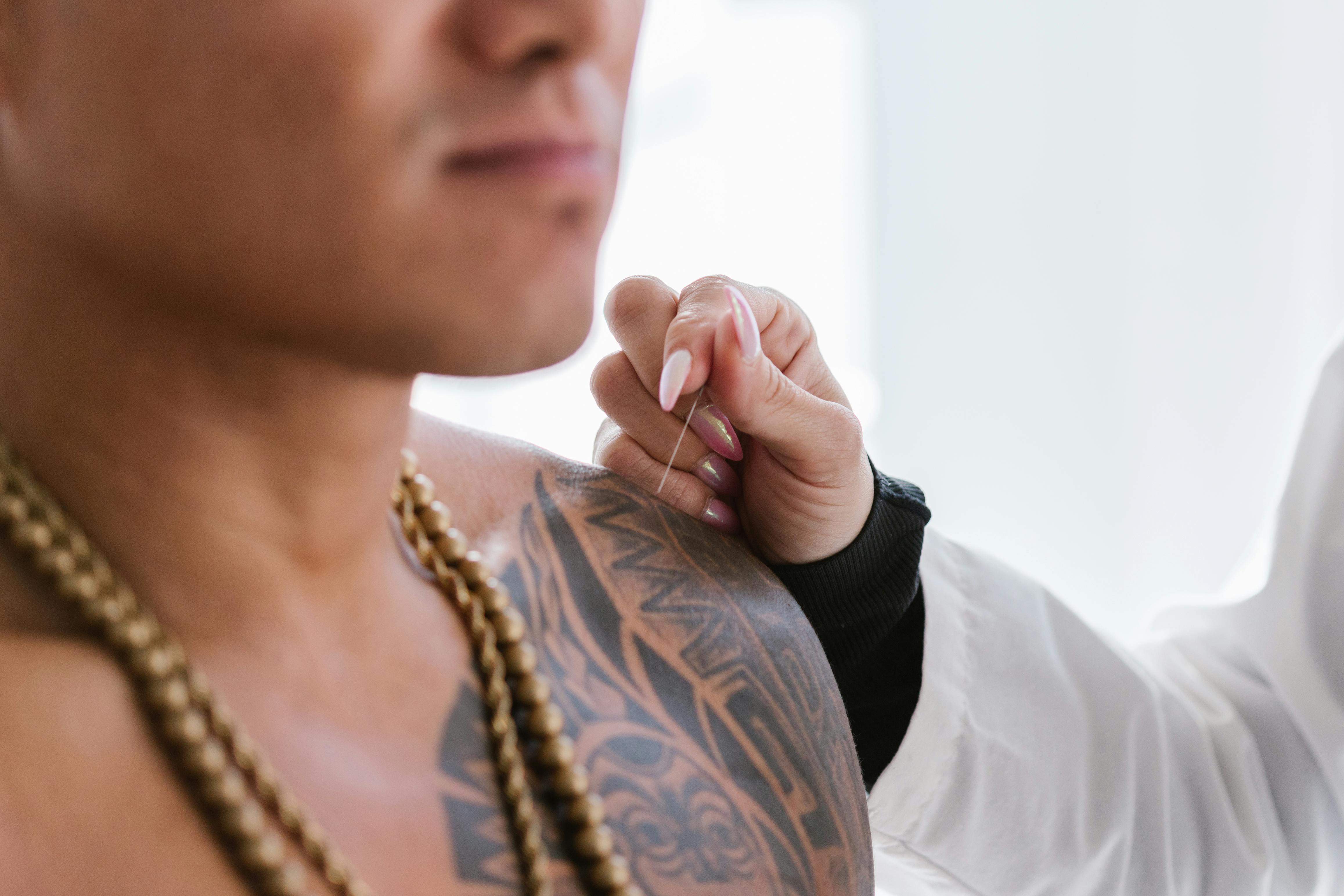 A hand holding a needle over the skin of a man with a tattoo
