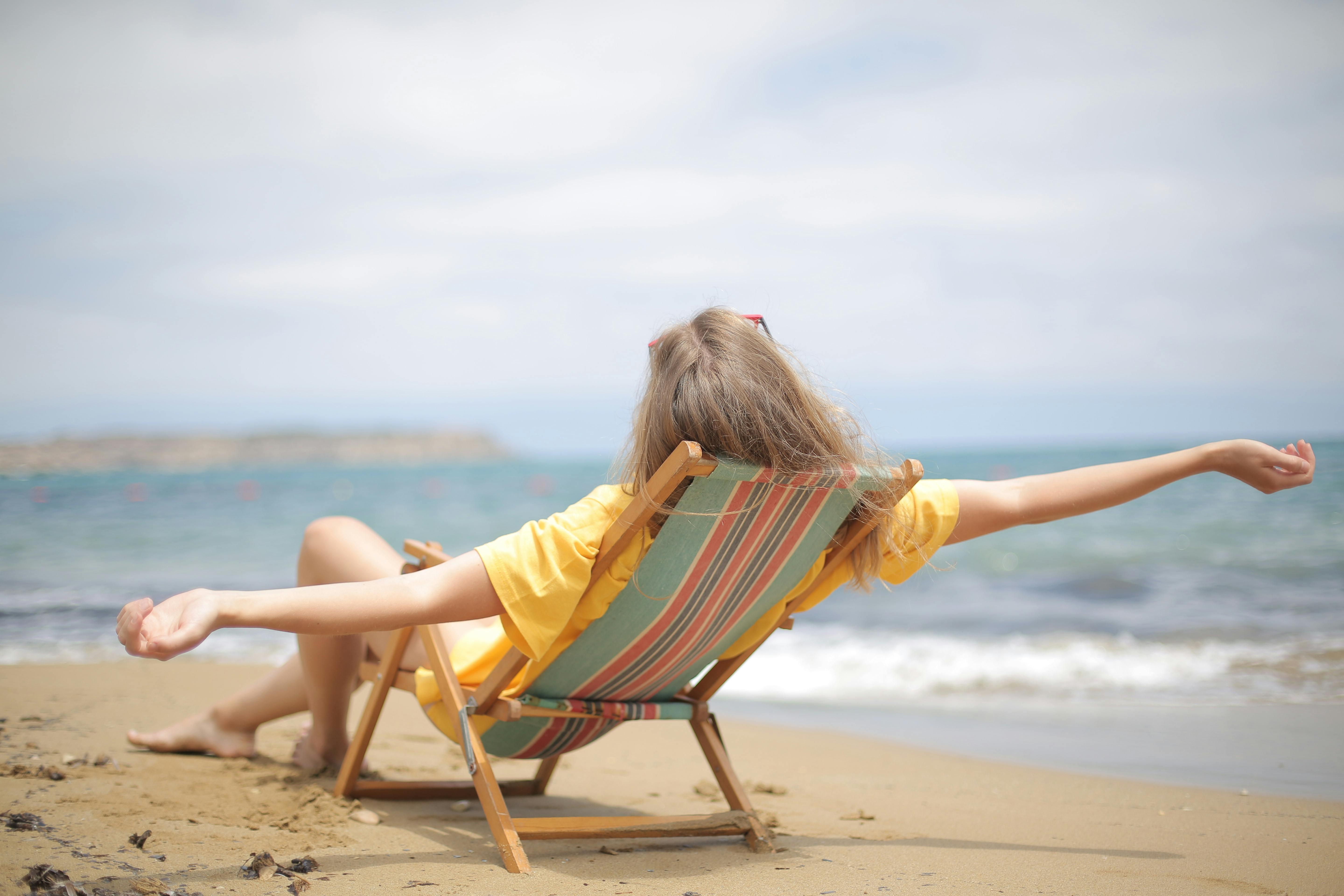 A woman relaxing on a folding chair by herself at an uncrowded beach.